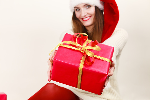 Christmas winter happiness concept. Smiling latin woman wearing santa helper hat holding present red gift box