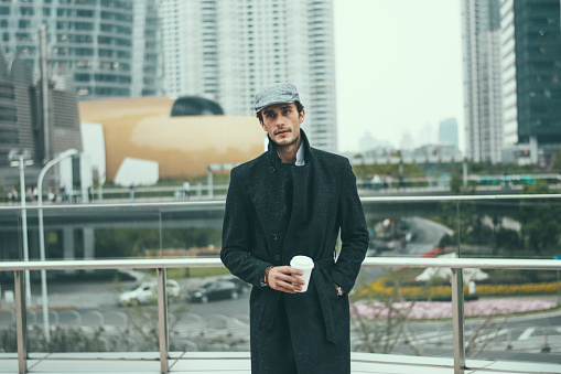 Young businessman in a winter coat, drinking coffee to go outdoors on a cold winter day, taking a break from work.