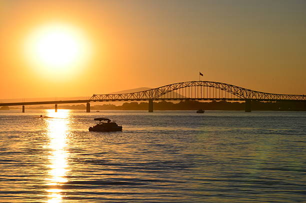A warm late afternoon looking into the setting sun as it starts to dip over the bridge, shedding its light across the water and silhouetting watercraft enjoying the relaxing afternoon.