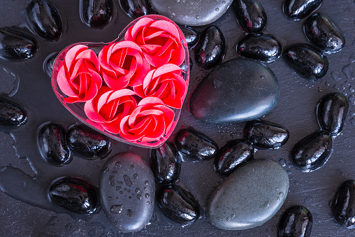rose flower soap shaped heart on black massage stones covered by water drops on slate top view