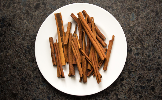 A pile of cinnamon sticks on a white plate, photographed on a kitchen countertop.