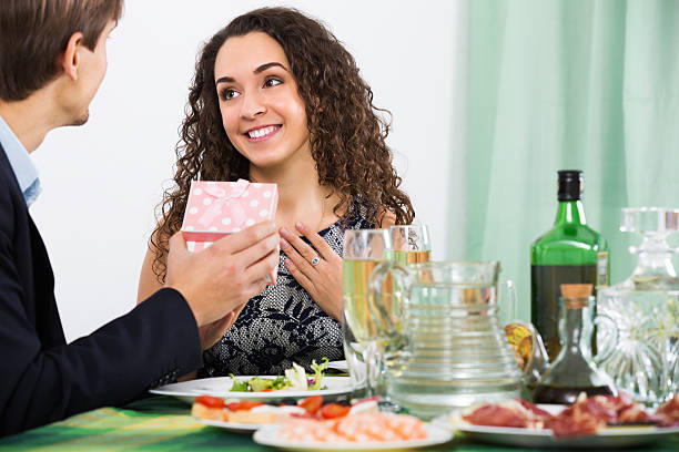Man giving present to woman Young man giving present to happy woman during romantic dinner in home wonderingly stock pictures, royalty-free photos & images