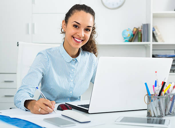 mujer feliz trabajando con papeleo y portátil - adminstrator fotografías e imágenes de stock