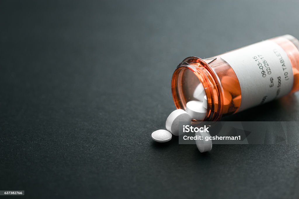 Pill bottle spilling out pills Red orange Pill bottle spilling out pills onto a black surface Prescription Medicine Stock Photo