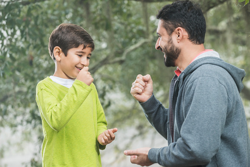 An Hispanic father playing with 7 year old boy. they are outdoors, at the park, playing a game of rock, paper, scissors.