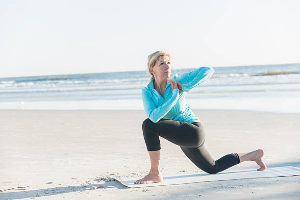 mature woman doing yoga exercises on beach - stretch beach imagens e fotografias de stock