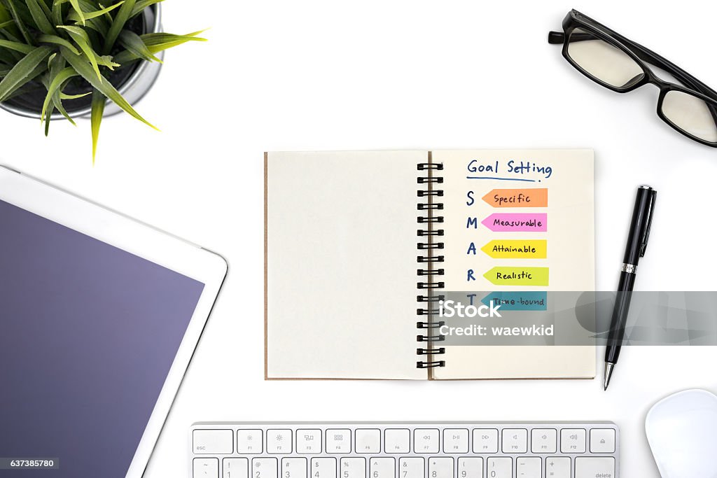 Smart goal setting with notebook Smart goal setting with notebook, eye glasses, pen, mouse, keyboard, tablet and plant on white desk, Success concept Intelligence Stock Photo