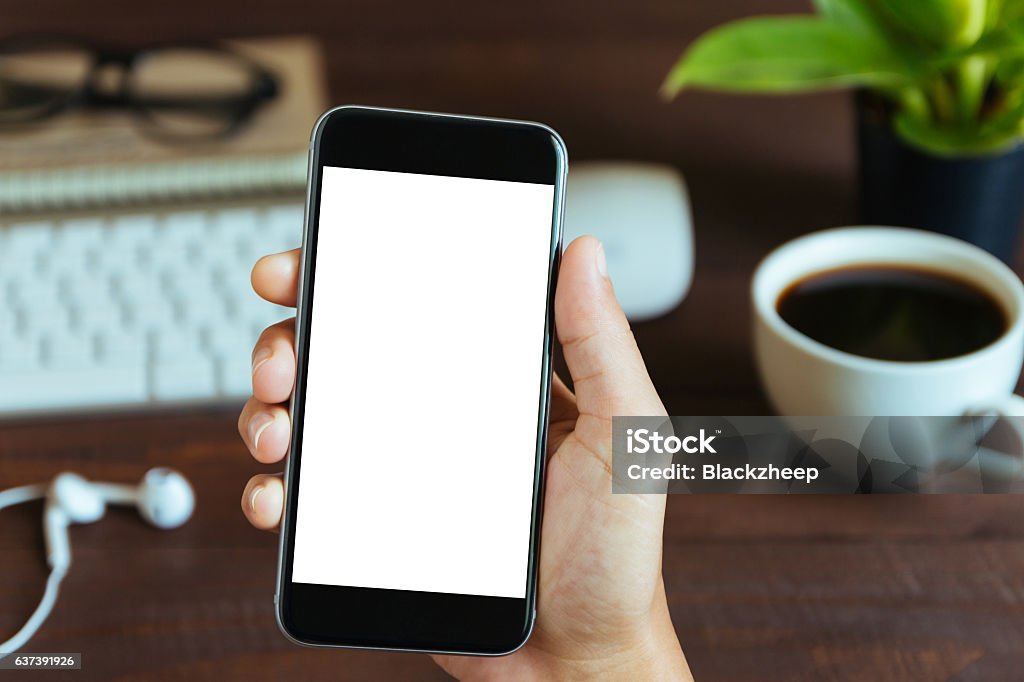 hand holding phone white screen over work table close-up hand holding phone white screen over work table Computer Monitor Stock Photo