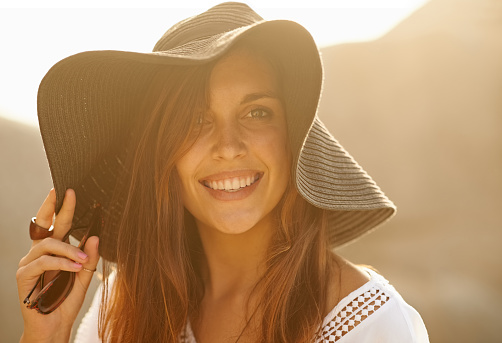 Portrait of a happy young woman wearing a hat while relaxing by the sea