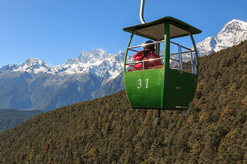 Lijiang, China - November 11, 2016: Cable Car on foreground with some tourists inside and Jade Dragon Snow Mountain on foreground. The Jade Dragon Snow Mountain, in Yunnan, it's the southernmost glacier in the northern emisphere.