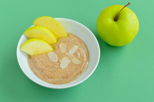 Yogurt almond butter with green apple for breakfast in a bowl on green background