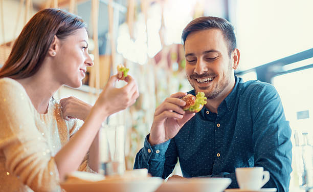 casal jovem bonito sentado em um café, tomando café da manhã - fast food restaurant restaurant cafe indoors - fotografias e filmes do acervo