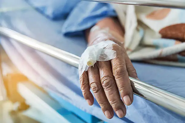 Close up hand of elderly patient with intravenous catheter for injection plug in hand during lying in the hospital bed