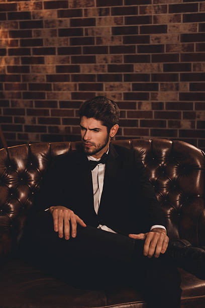 istock Imposing young man in elegant black suit sitting on couch 637412412