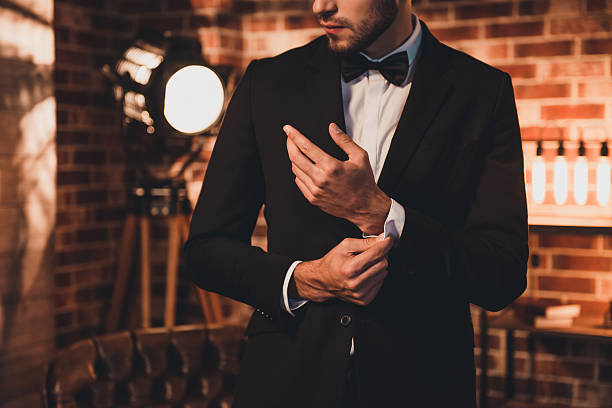 nahaufnahme des stilvollen mannes in schwarzem anzug, der manschettenknöpfe befestigt - smoking issues fotos stock-fotos und bilder