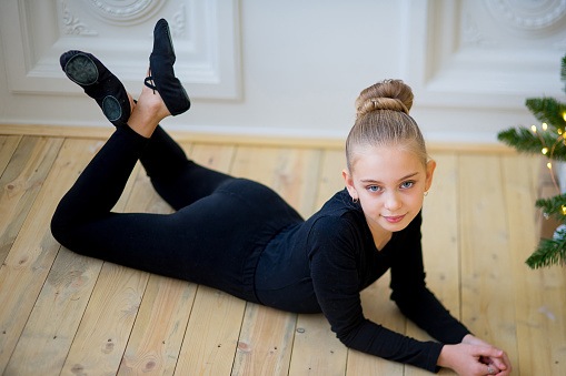 Young ballet dancer in the black clothes lying near the wall on the wooden floor