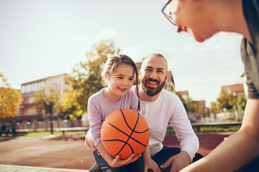 Young family on an outdoors basketball field, playing the game and having fun together