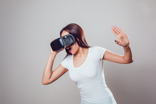 Attractive woman using virtual reality goggles on grey background. VR headset.