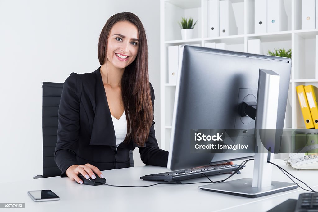 Portrait of successful business lady Smiling businesswoman with long dark hair is working at her personal computer in white office with yellow and green binders. Concept of successful business person File Clerk Stock Photo