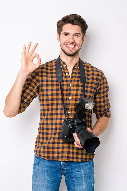Portrait of handsome cheerful photographer  with camera gesturing ok