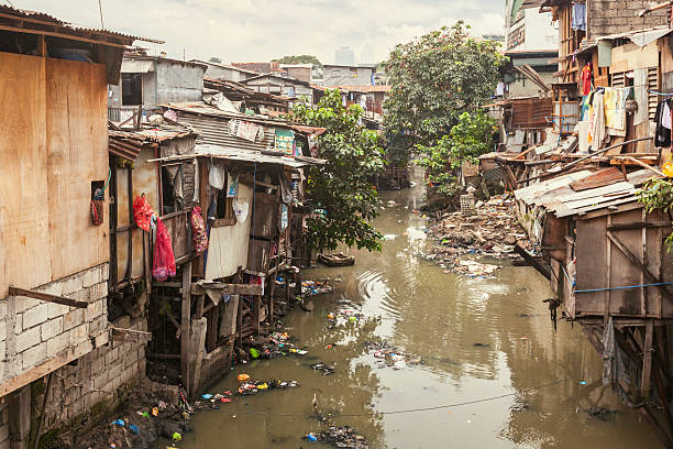 baracche lungo un canale inquinato - povertà asia foto e immagini stock