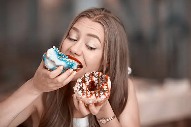 cute young woman holding donuts and biting it.cravinf for sweets.horizontal lifestyle shot.