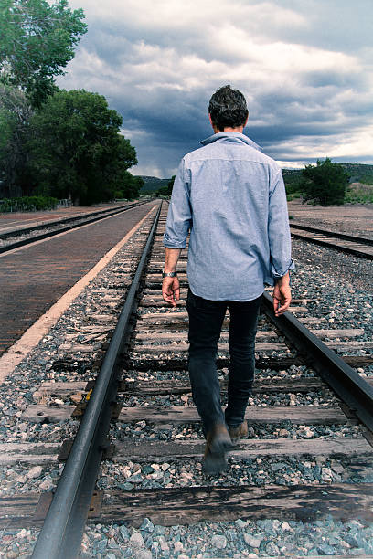 istock Walking the Rails: Man Walks on Track Toward Stormy Sky 637502410