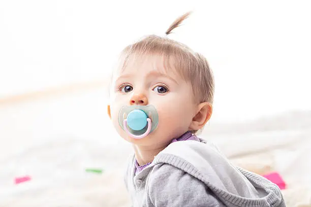 little infant girl with her blue pacifier and a funny tuft posing as a fashion model