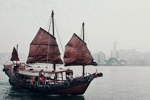 Traditional Chinese sailing ships with red sails in Victoria harbor at sunset.