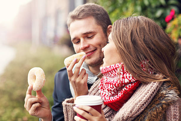 istock Young couple sitting on bench with coffee and donuts 637513050