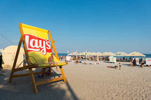 Odessa, Ukraine - September 7, 2016: A young man relaxes in a giant Lay's branded chair at the beach in Odessa, Ukraine.