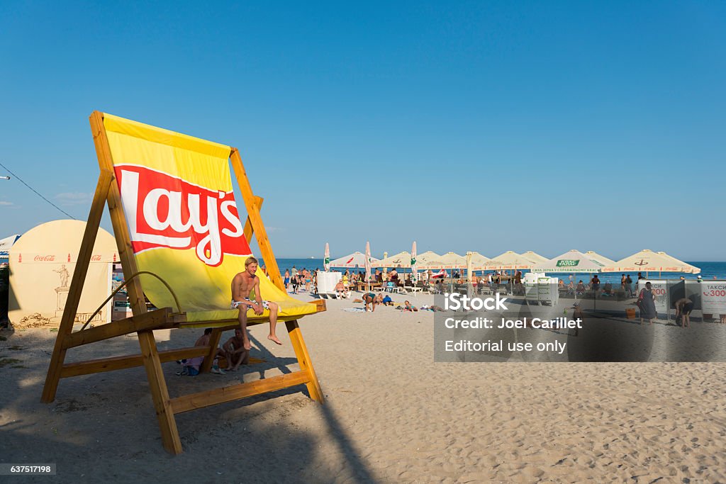 Beach life in Odessa, Ukraine Odessa, Ukraine - September 7, 2016: A young man relaxes in a giant Lay's branded chair at the beach in Odessa, Ukraine. Chair Stock Photo