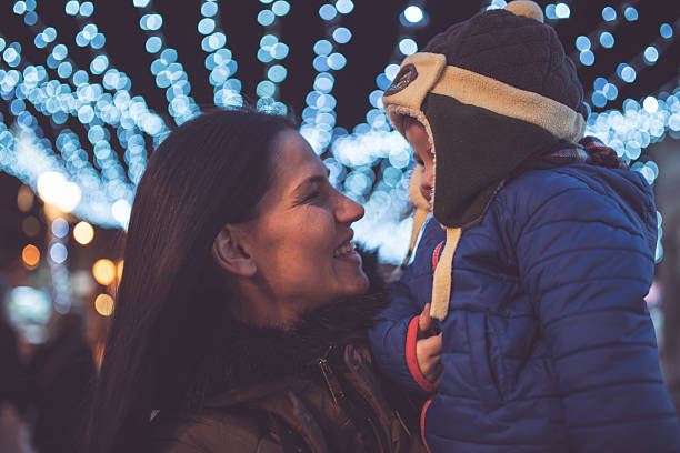 Mother holding her baby boy under the christmas light decoration in the city
