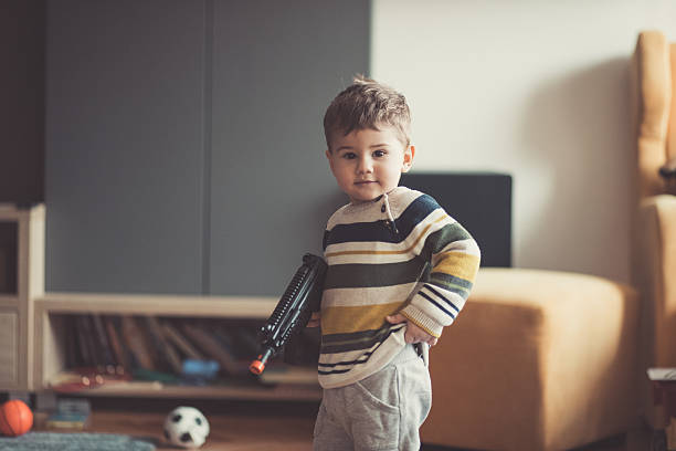 Me as a shooter Baby boy holding a toy gun and posing in the livingroom baby gun stock pictures, royalty-free photos & images