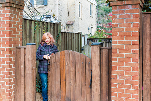 Young woman opening wooden fence door in neighborhood in autumn