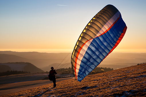 Wasserkuppe, Germany - December 29, 2016: A male paraglider prepares his equipment and parachute at Wasserkuppe, Germany on a cold winter evening. The Wasserkuppe is a mountain in the Rhoen mountains (950m) and well-known as a perfect place for paragliding and sailplane activities.