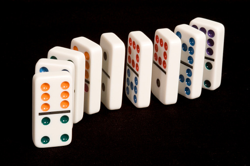 A curved line of colorful dominoes on a black background, with an orange and green six and four game piece in the foreground