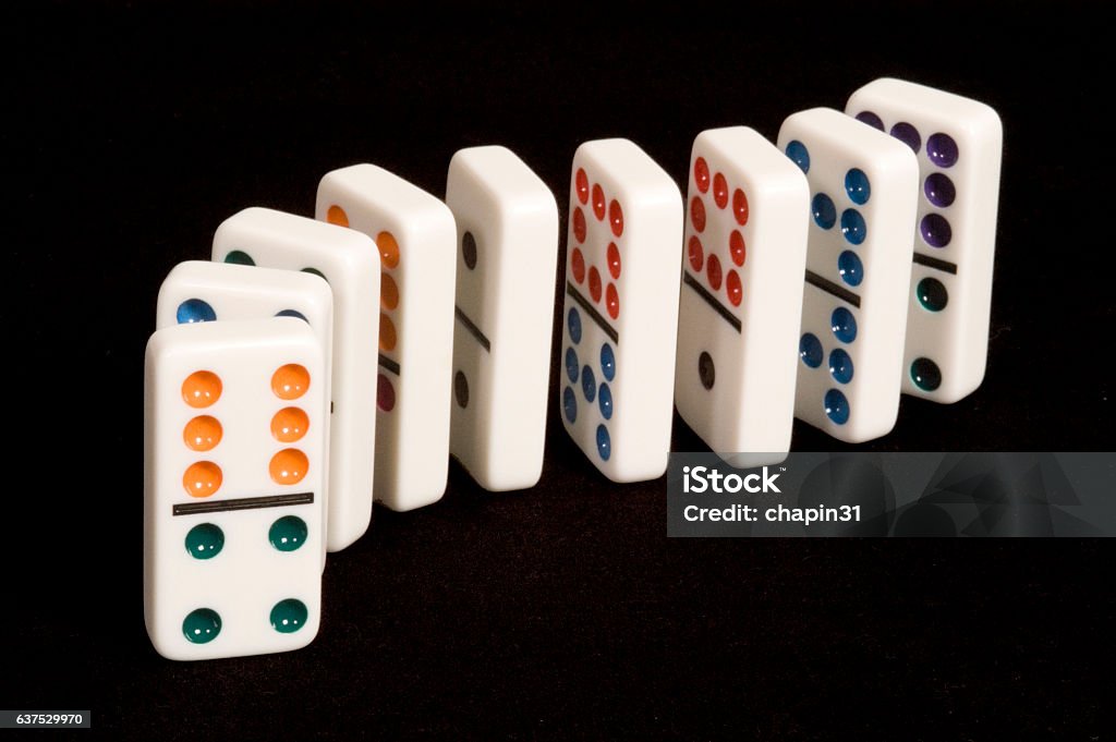 Dominoes in a Curved Line A curved line of colorful dominoes on a black background, with an orange and green six and four game piece in the foreground Domino Stock Photo