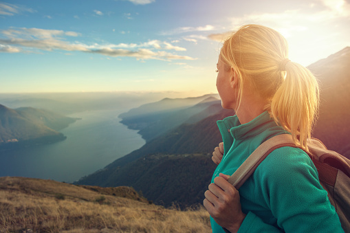 Young woman hiking reaches the mountain top, contemplates the spectacular landscape.