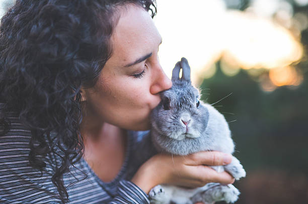 A pet owner is kissing her pet rabbit outdoors during summer