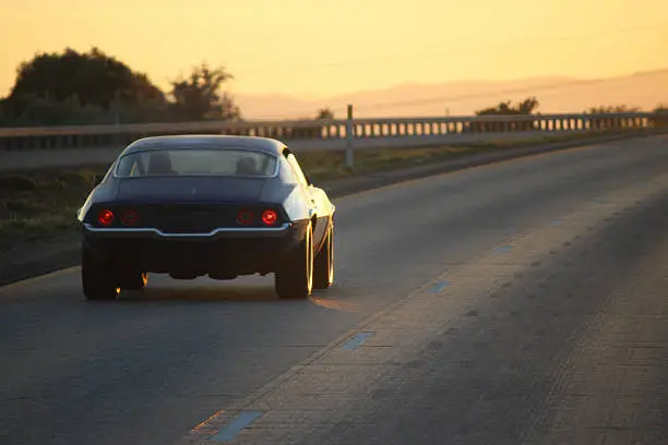 Classic car cruising into the sunset on the open road.