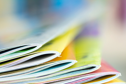 Close up edge of colorful magazine stacking with  blurry bookshelf background for publication and publishing concept , extremely DOF