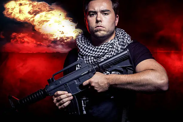 Soldier with a gun surviving bombs that are weapons of mass destruction or a nuclear war. The image depicts warfare and apocalyptic WW3.  The man with a rifle represents a military troops or private military contractor mercenary.