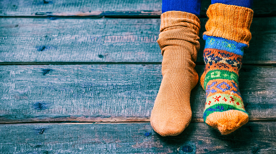 Female feet wearing odd wool socks on the wooden floor. Closeup view