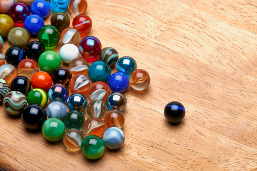 Lot of Multi colored Marbles on wooden board. Concept of standing out of the crowd