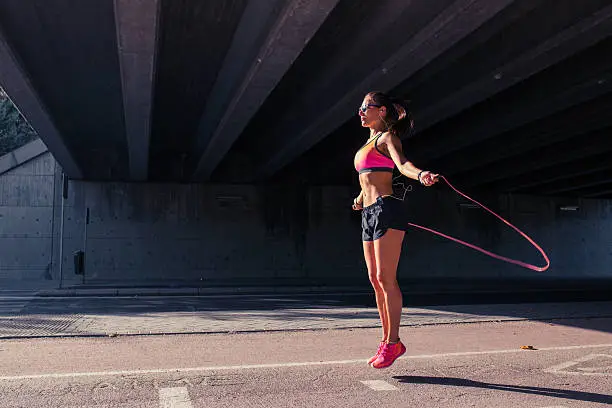 Fit athletic woman runner doing her warming up routine exercises with jumping rope outdoors