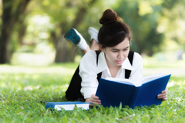 istock Smiling casual Asian student lying on grass reading book. 637580522