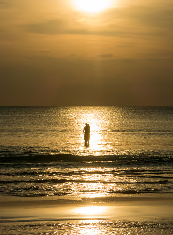 Koh Lanta, Thailand - November 16, 2016: A young man and woman have a romantic embrace in the sunset shallow waters of the Andaman Sea, Thailand.  The image conveys peace and togetherness. This image was taken on Koh Lanta public beach, Krabi, Thailand.