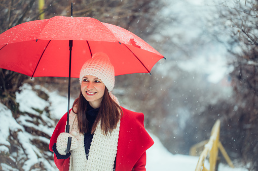 Woman in red coat with red umbrella enjoying the lovely first day of snow outdoors.