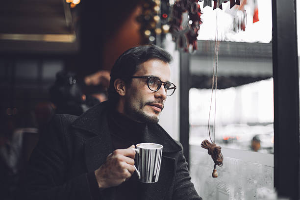 Looking outside Bearded hipster sitting in the cafe, enjoying a nice hot cup of coffee on a cold winter day. rainy cafe stock pictures, royalty-free photos & images